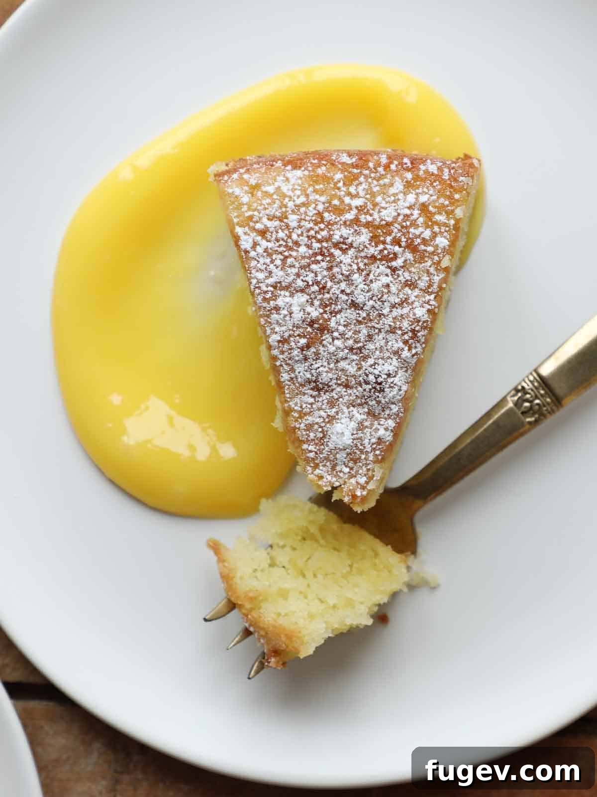 Zesty Mediterranean Olive Oil Cake 12 powdered sugar on slice of olive oil cake on white plate with lemon curd.