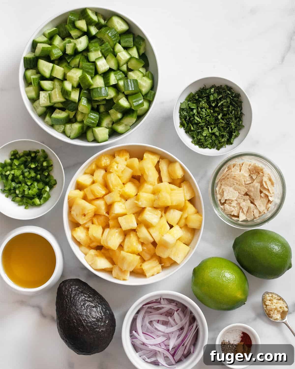 Refreshing Pineapple Cucumber Medley 3 A vibrant flat lay of all the fresh ingredients for pineapple cucumber salad, including diced pineapple, sliced cucumbers, whole limes, red onions, tortilla chips, avocado, jalapeños, garlic, and various seasonings.