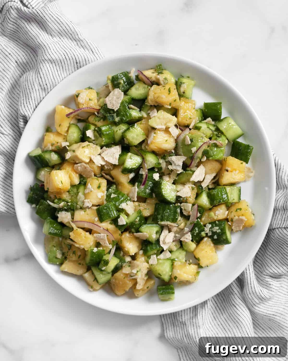 Refreshing Pineapple Cucumber Medley 6 A single serving of pineapple cucumber salad elegantly plated, garnished with a sprig of mint and a lime wedge, highlighting its fresh appeal.