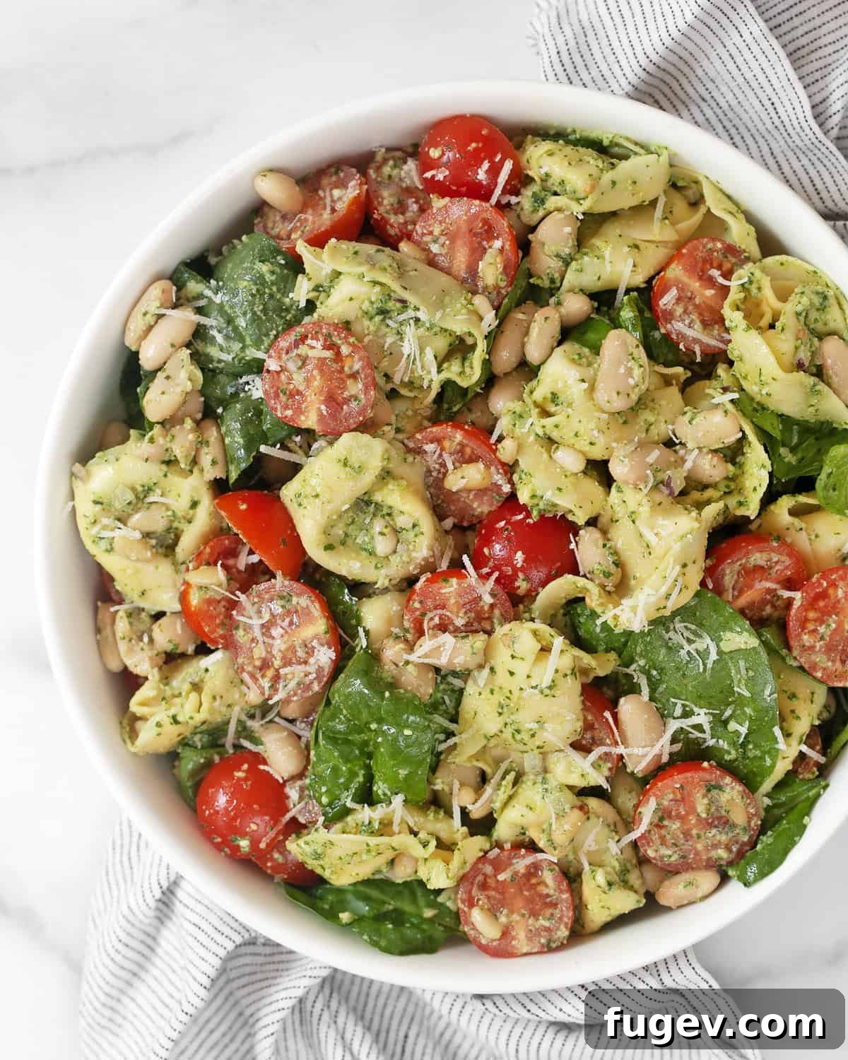 Vibrant Pesto Tortellini Salad with Cannellini and Cherry Tomatoes 2 A vibrant bowl of pesto tortellini pasta salad, garnished with fresh basil leaves and parmesan cheese, ready to be served.