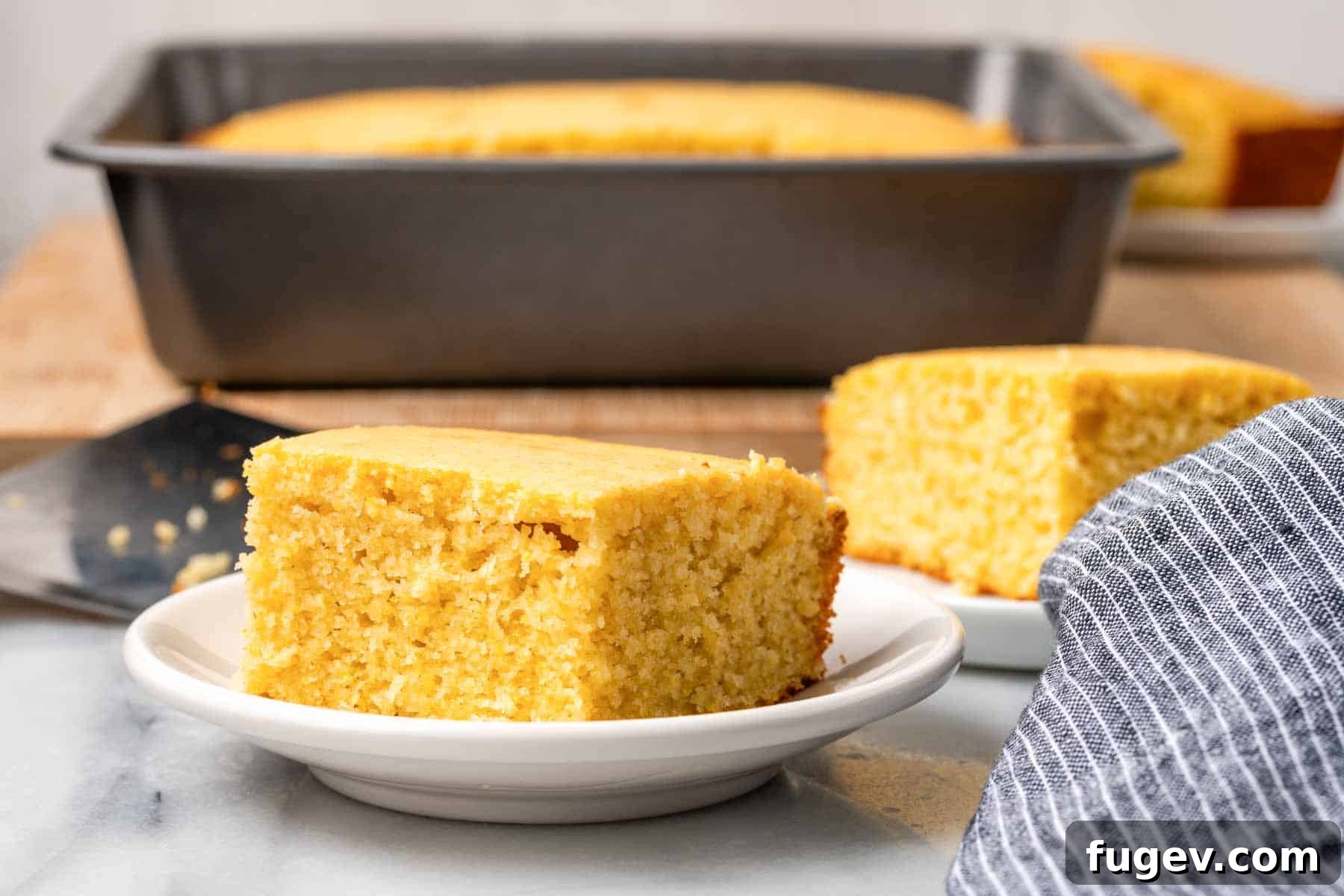 Sweet Cornbread Perfection 3 sweet cornbread slices on white plates with baking dish in background.