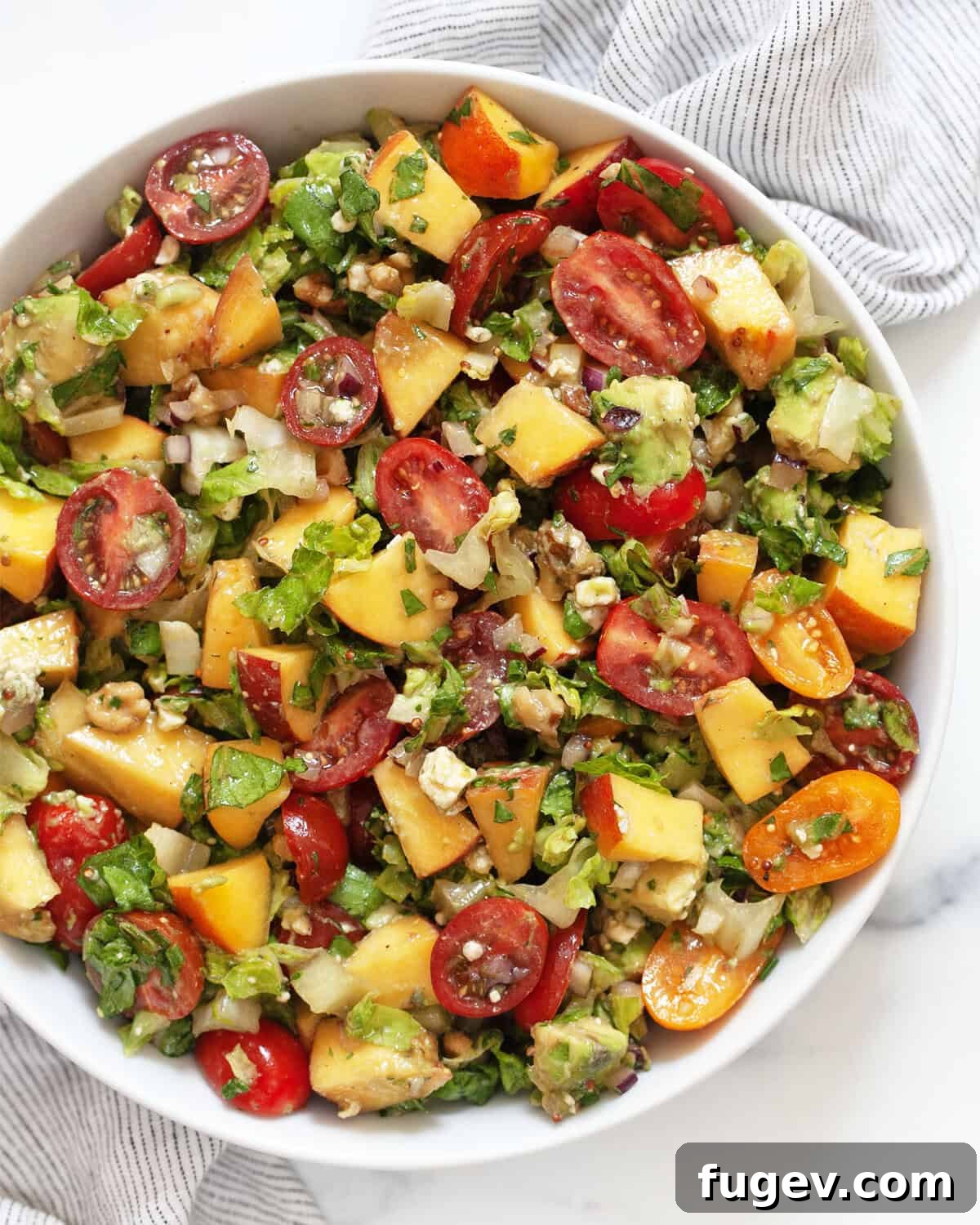 Sunshine Chopped Salad 2 A vibrant summer chopped salad in a large bowl, showcasing peaches, tomatoes, and avocados mixed with greens.