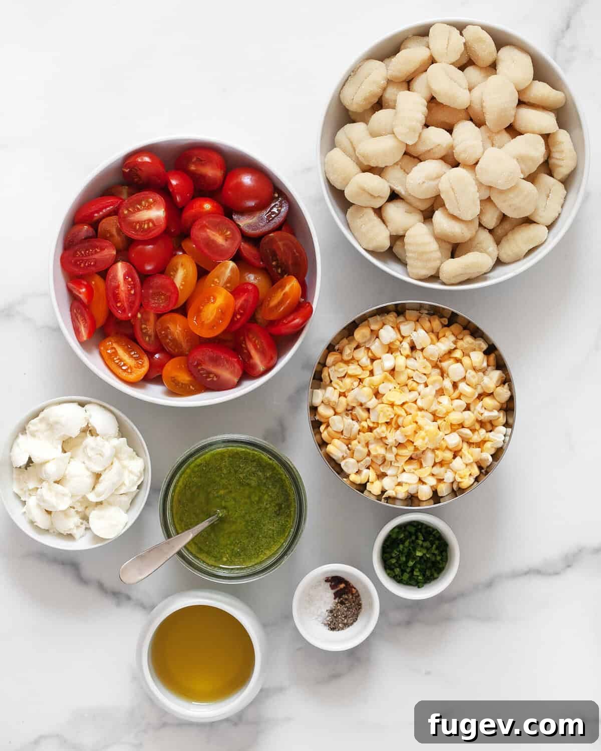 Roasted Gnocchi with Burst Tomatoes and Sweet Corn 3 Ingredients including gnocchi, tomatoes, corn, pesto, mozzarella, olive oil, chives, red pepper flakes, salt and pepper laid out on a table.