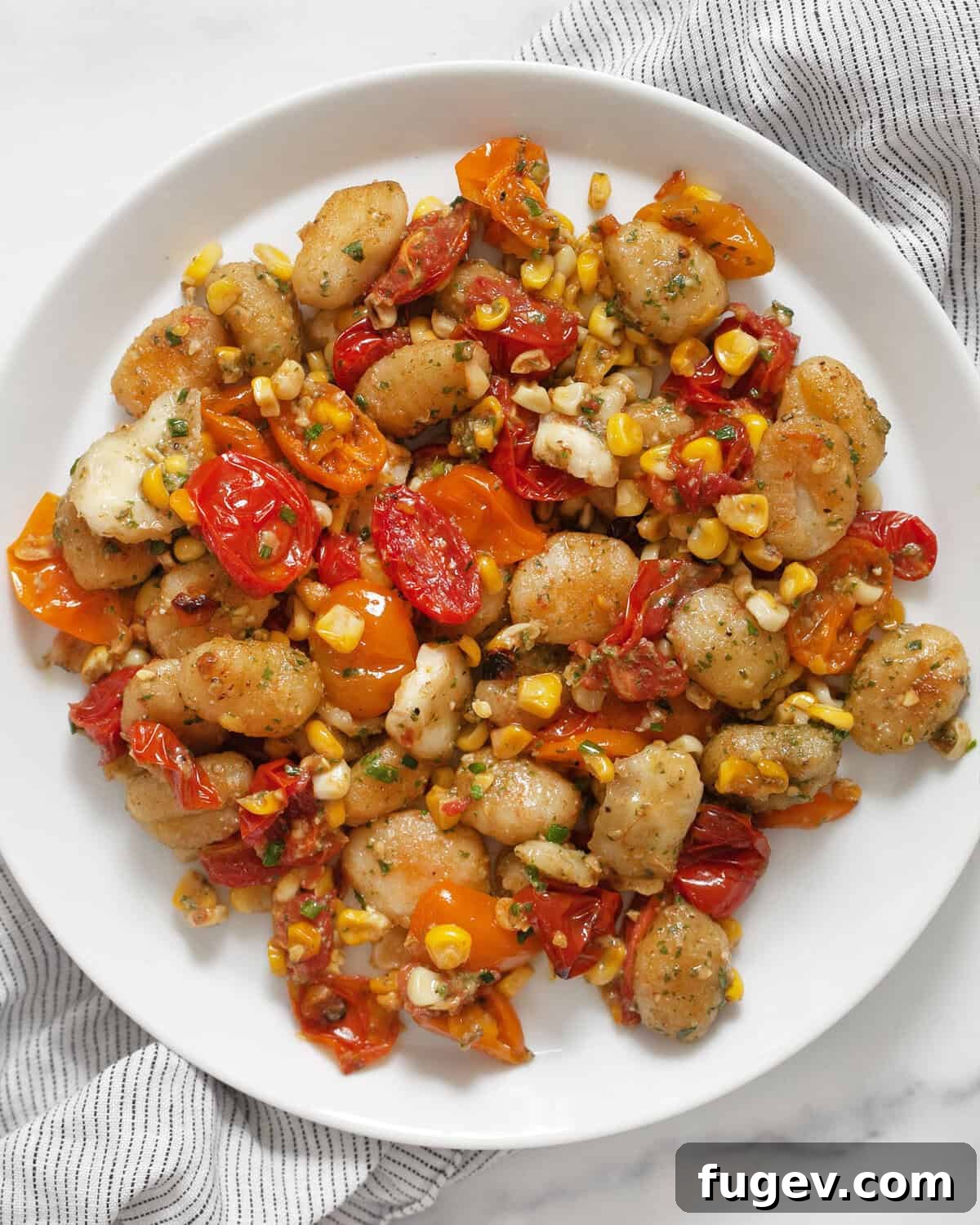 Roasted Gnocchi with Burst Tomatoes and Sweet Corn 6 Sheet pan gnocchi with tomatoes and corn on a plate, garnished with fresh herbs.