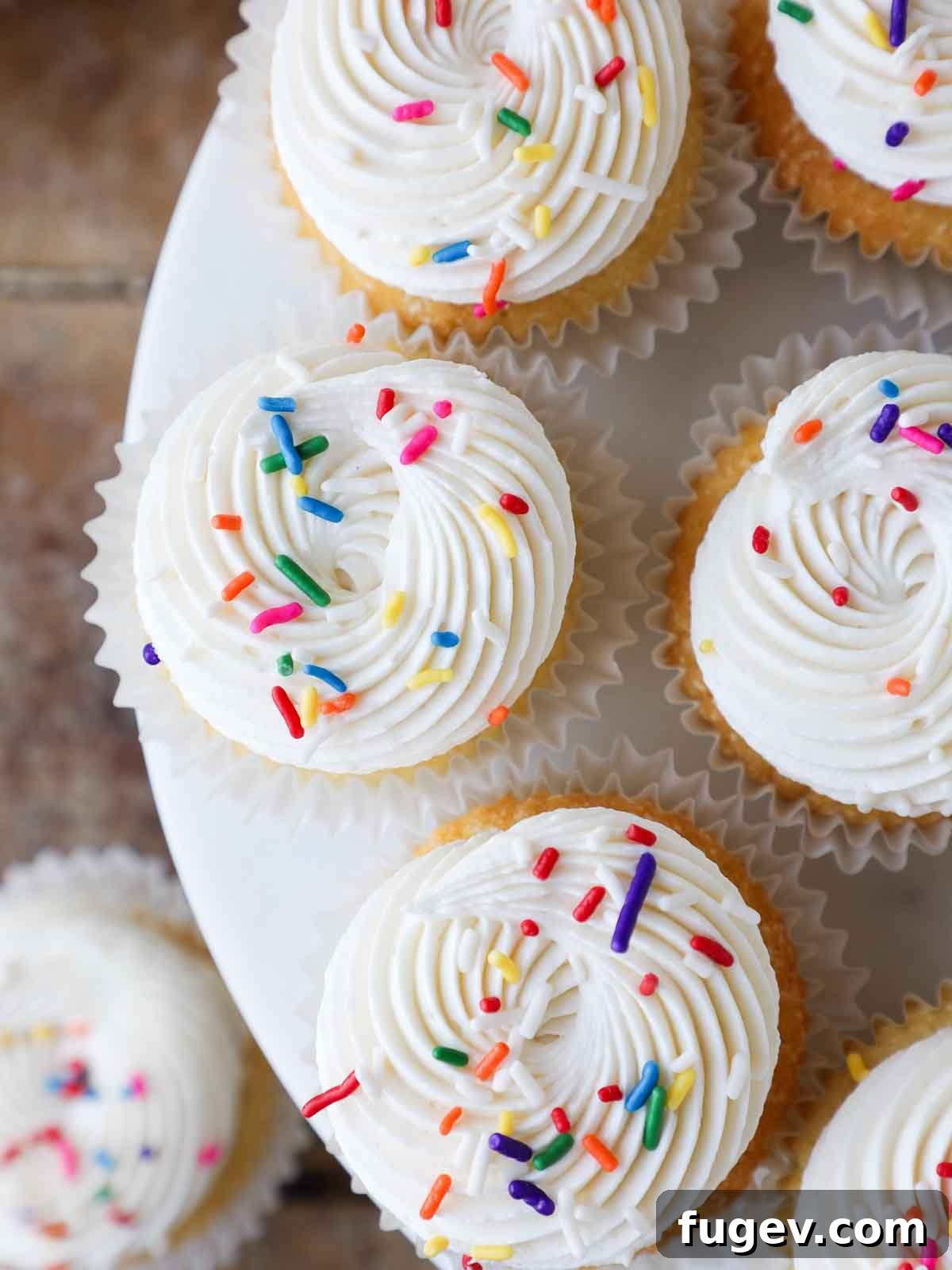 Golden Vanilla Bliss 3 Beautifully piped ermine frosting adorned with colorful sprinkles on soft vanilla cupcakes.