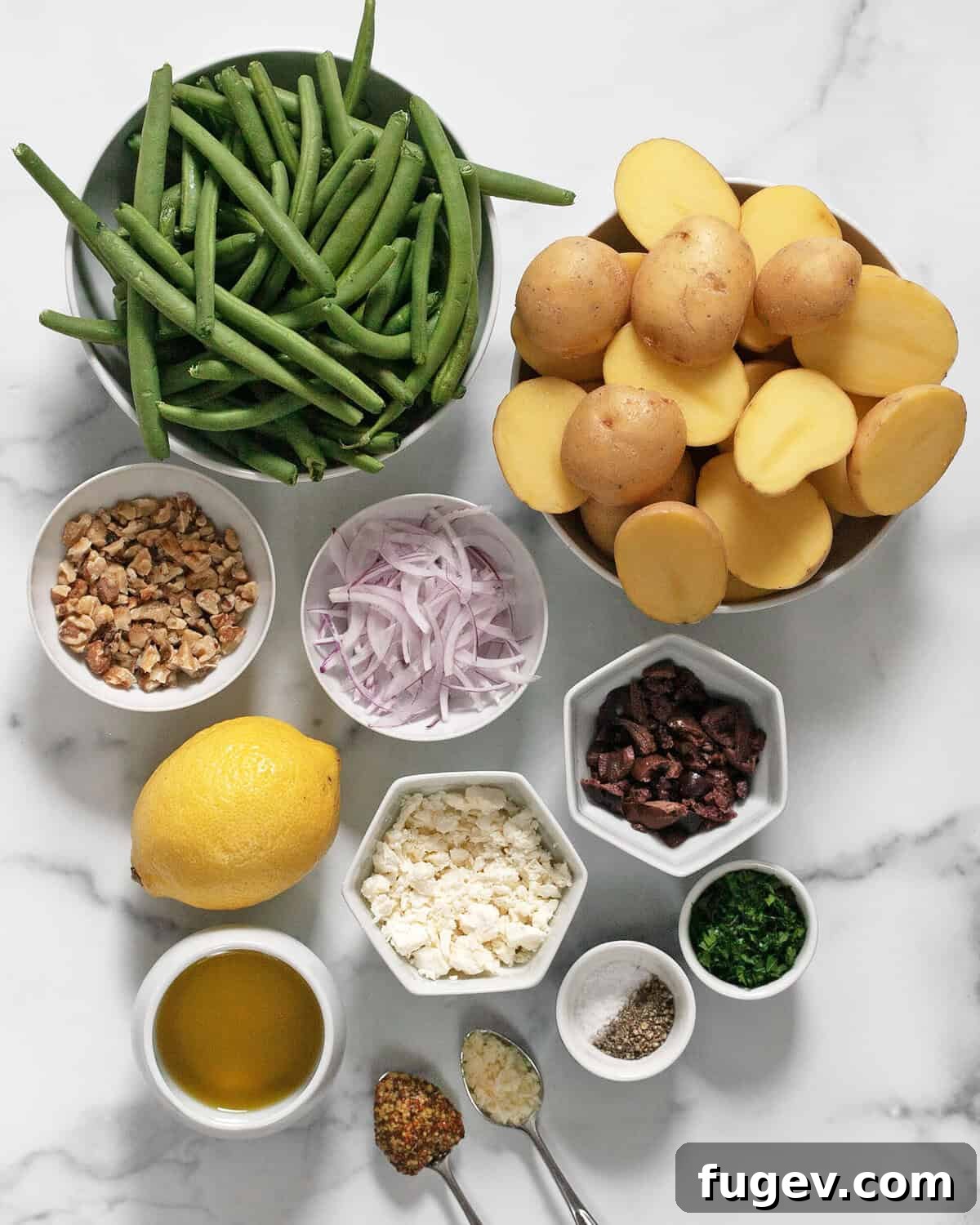 Rustic Roasted Potato and Green Bean Salad 3 A flat lay image displaying all the fresh ingredients for roasted potato and green bean salad: baby potatoes, green beans, red onions, Kalamata olives, fresh lemon, crumbled feta, olive oil, and parsley.