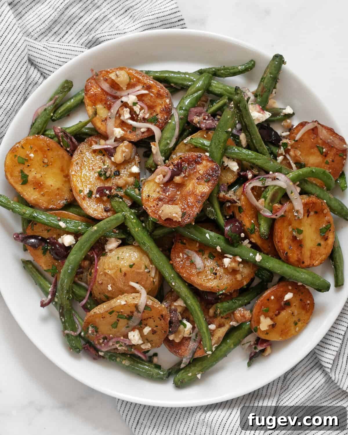 Rustic Roasted Potato and Green Bean Salad 7 A single serving of roasted potato and green bean salad neatly arranged on a white plate, showcasing its appealing colors and textures, garnished with fresh parsley.