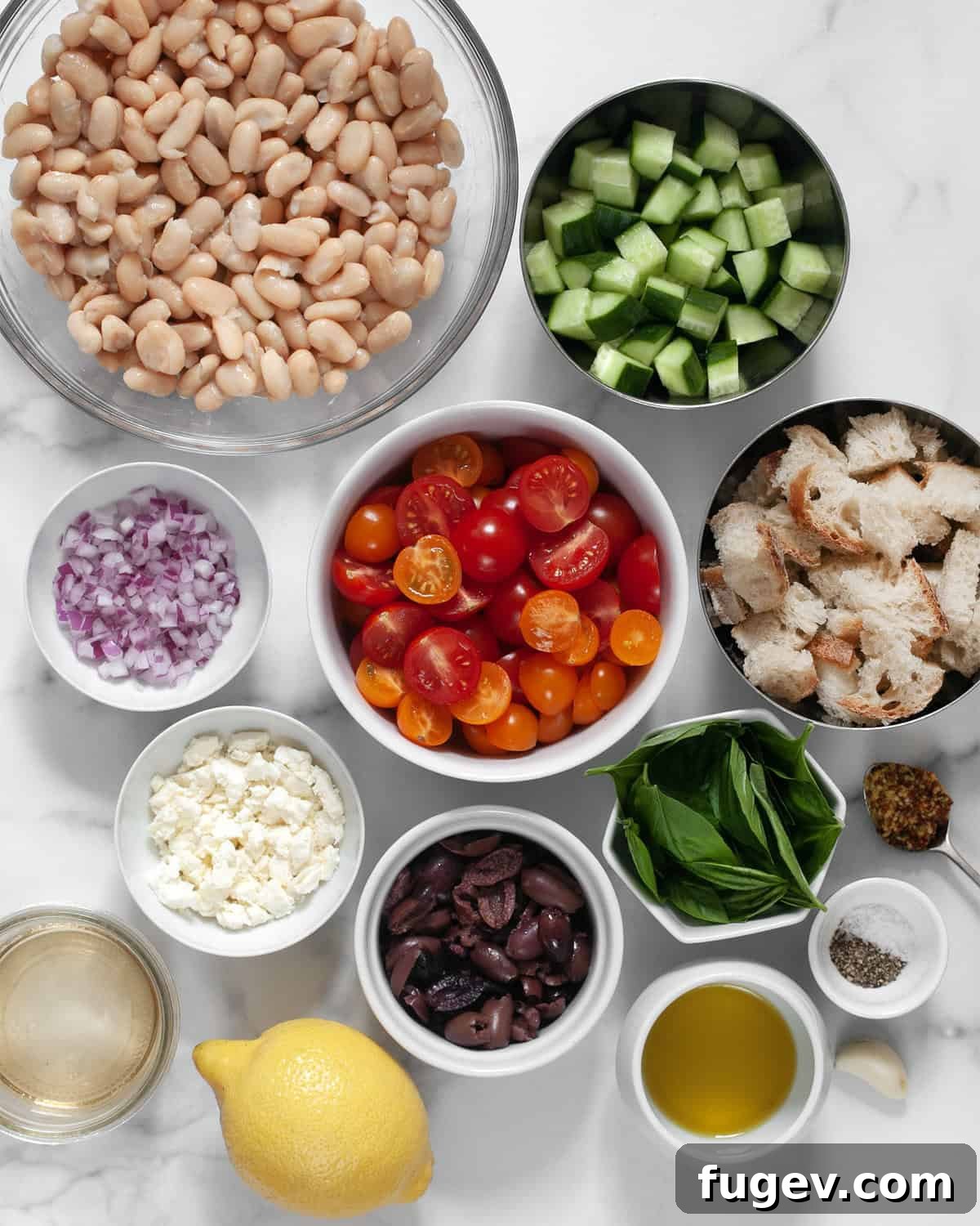 Tuscan White Bean Salad 3 A flat lay of all ingredients for cannellini bean salad including cannellini beans, tomatoes, cucumbers, olives, feta, red onions, basil, lemon, white wine vinegar, olive oil, salt and pepper.