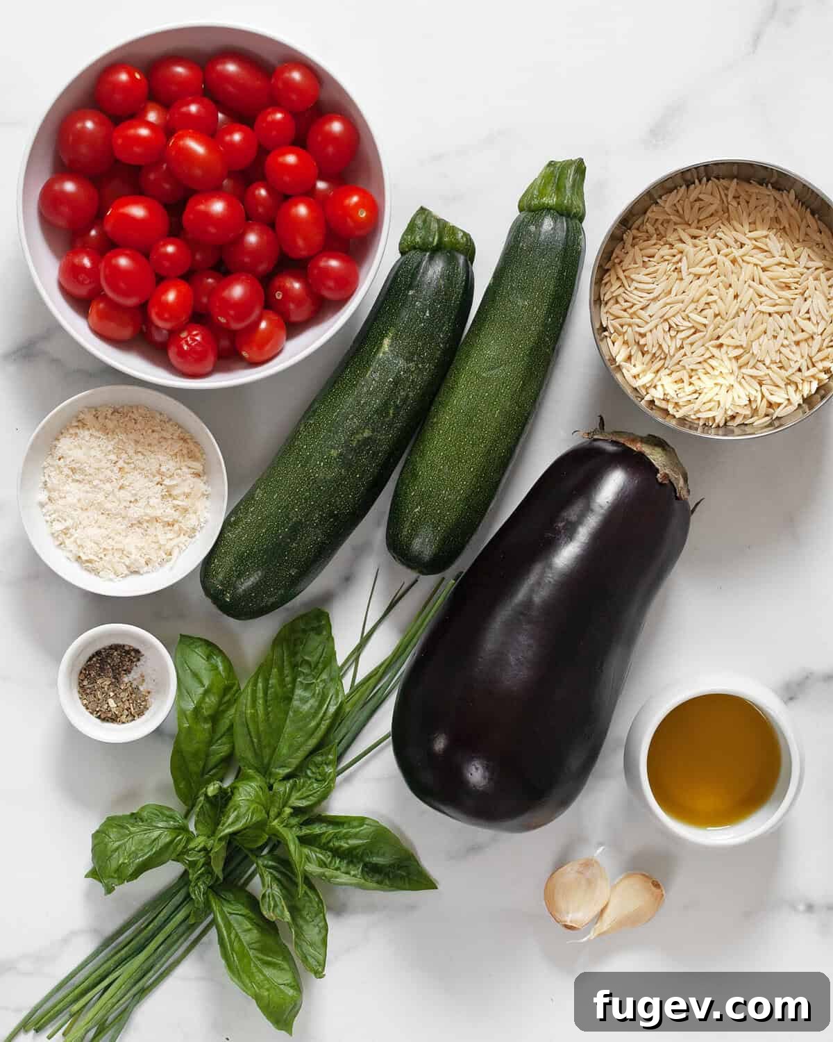 Roasted Mediterranean Vegetable Orzo 3 A vibrant display of fresh ingredients for the orzo recipe, including eggplant, zucchini, tomatoes, orzo pasta, basil, chives, parmesan cheese, olive oil, Italian seasoning, garlic, salt, and pepper.