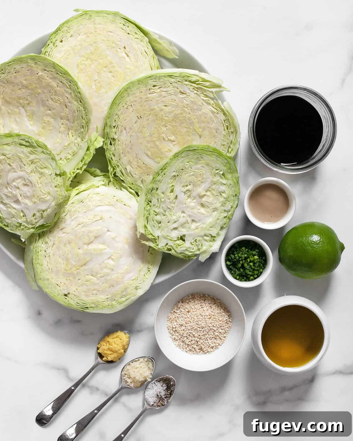 Smoky Grilled Cabbage Steaks 3 A flat lay photograph showcasing all the ingredients for grilled cabbage steaks: a head of green cabbage, a bowl of tahini, a bottle of soy sauce, fresh ginger, garlic, lime, olive oil, sesame seeds, salt, pepper, and fresh herbs like cilantro.