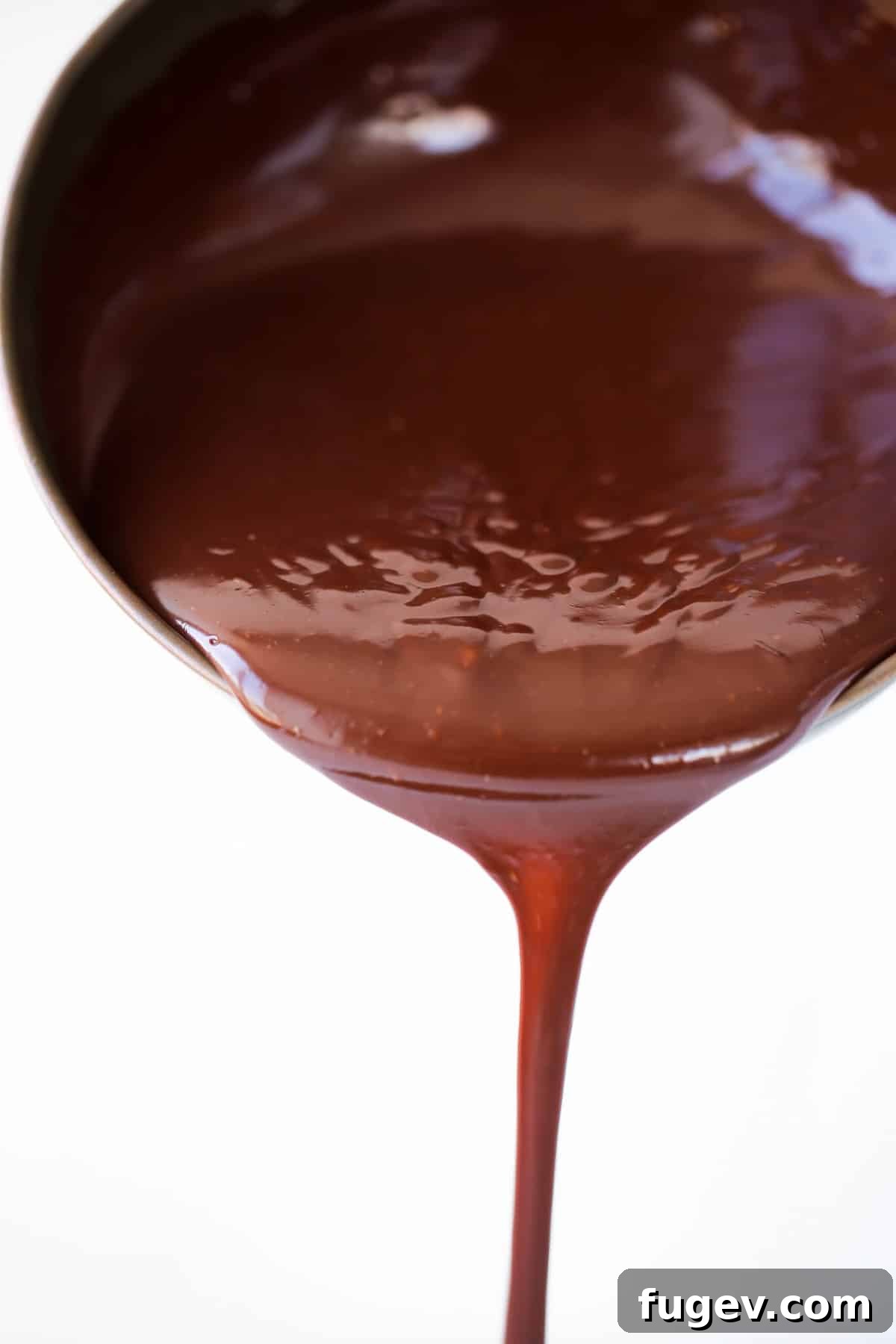 Mastering Chocolate Ganache 2 Silky chocolate ganache pouring in one stream from a copper pot, ready to elevate any dessert.