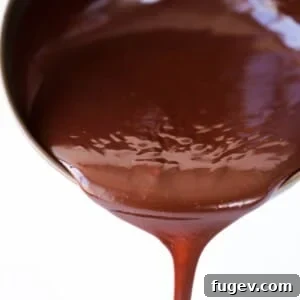 Silky chocolate ganache pouring in one stream from a copper pot, highlighting its perfect consistency.