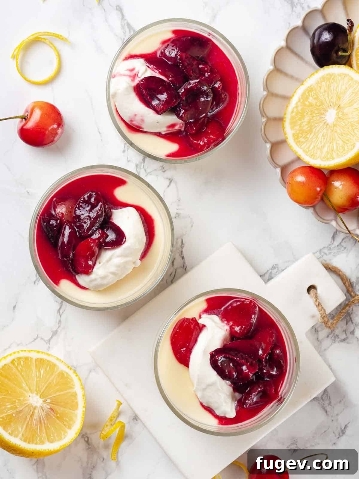 Zesty Lemon Cream 11 Three perfectly set lemon possets in glasses, generously topped with fluffy whipped cream and a rich, vibrant cherry sauce, ready to be served.