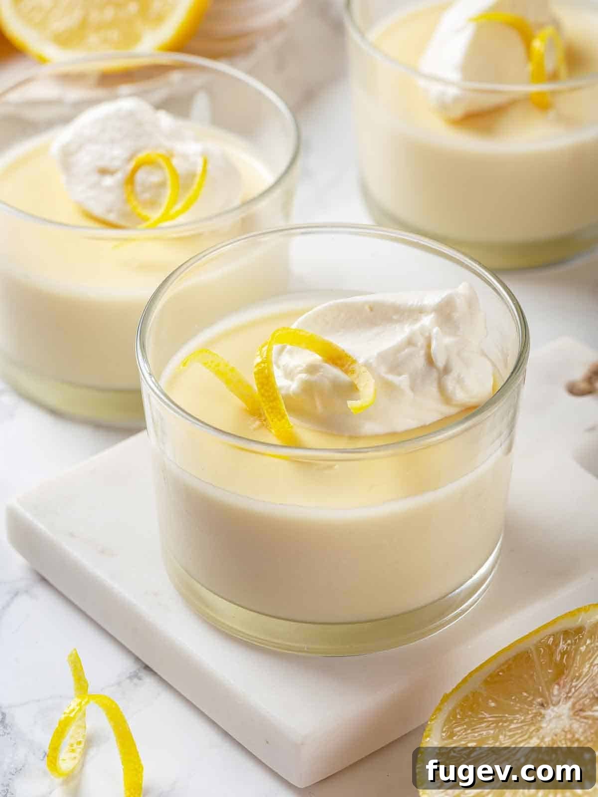 Zesty Lemon Cream 12 Three lemon possets in clear dessert glasses, each artfully topped with a swirl of fresh whipped cream, ready to be served.
