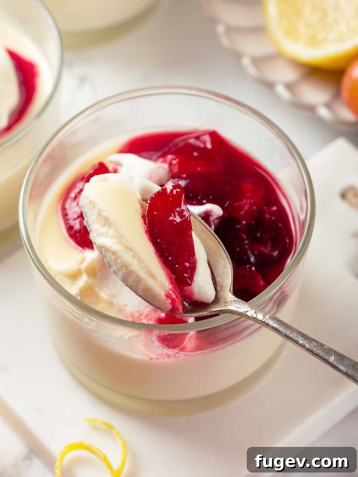 Zesty Lemon Cream 3 A silver spoon holding a generous bite of lemon posset, topped with glossy cherry sauce, highlighting the dessert's smooth texture and vibrant colors.