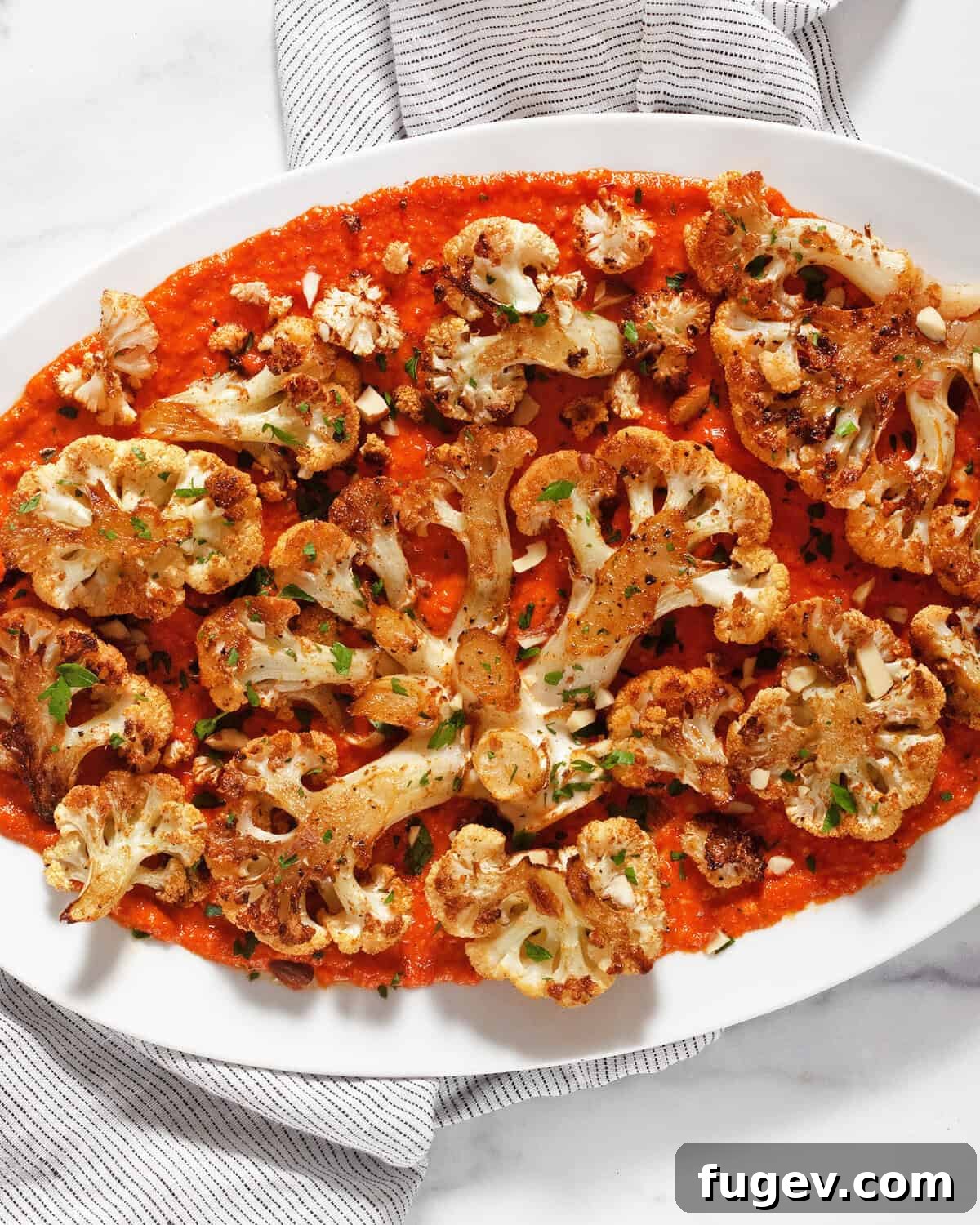 Pan-Seared Portobello Mushroom Steaks 2 Flavorful roasted cauliflower steaks served on a platter with bright red pepper pesto, garnished with fresh herbs and almonds.