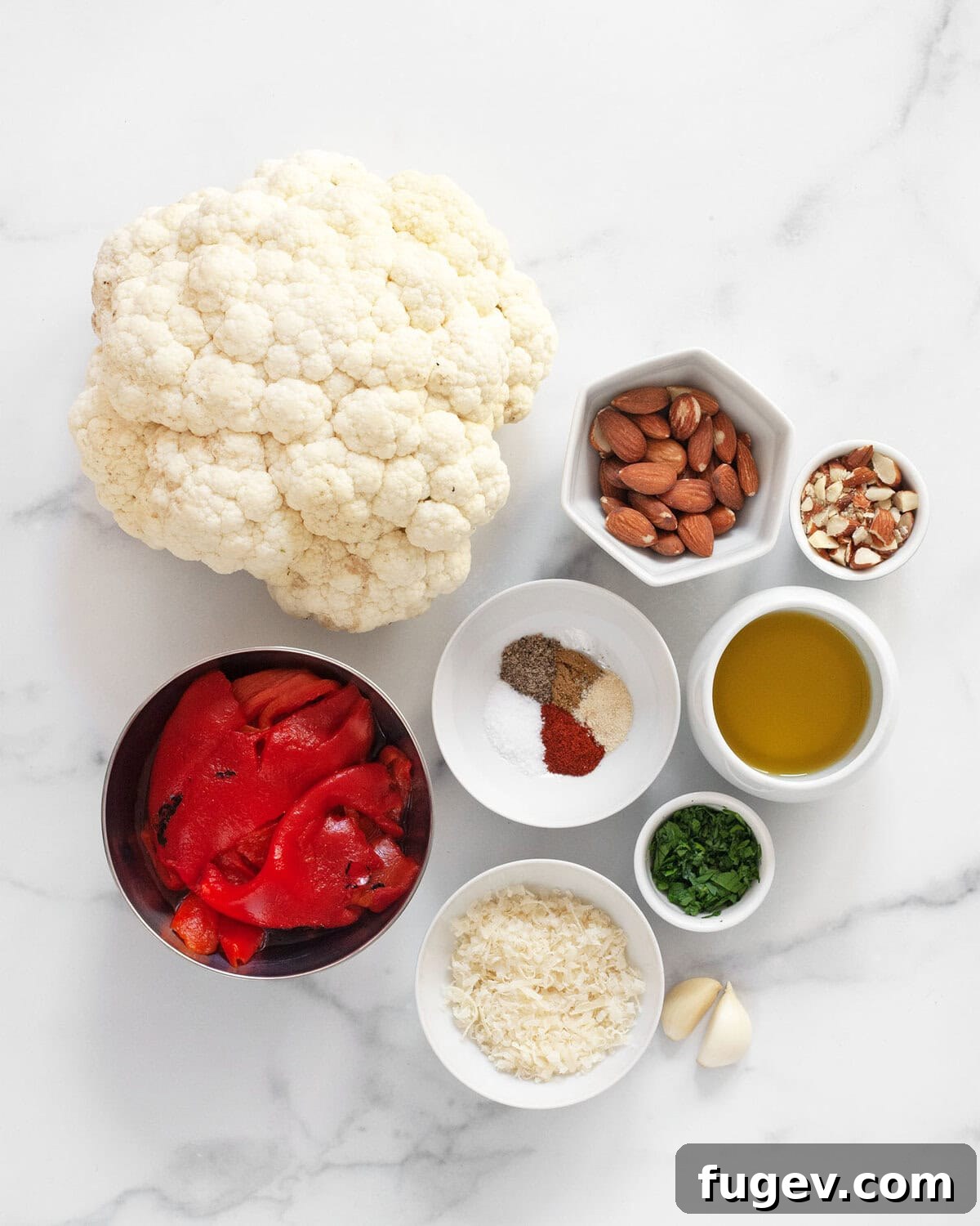 Pan-Seared Portobello Mushroom Steaks 3 A selection of fresh ingredients including a whole cauliflower head, olive oil, a variety of seasonings, fresh parsley, garlic cloves, Parmesan cheese, almonds, and jarred roasted red peppers, laid out on a kitchen surface.