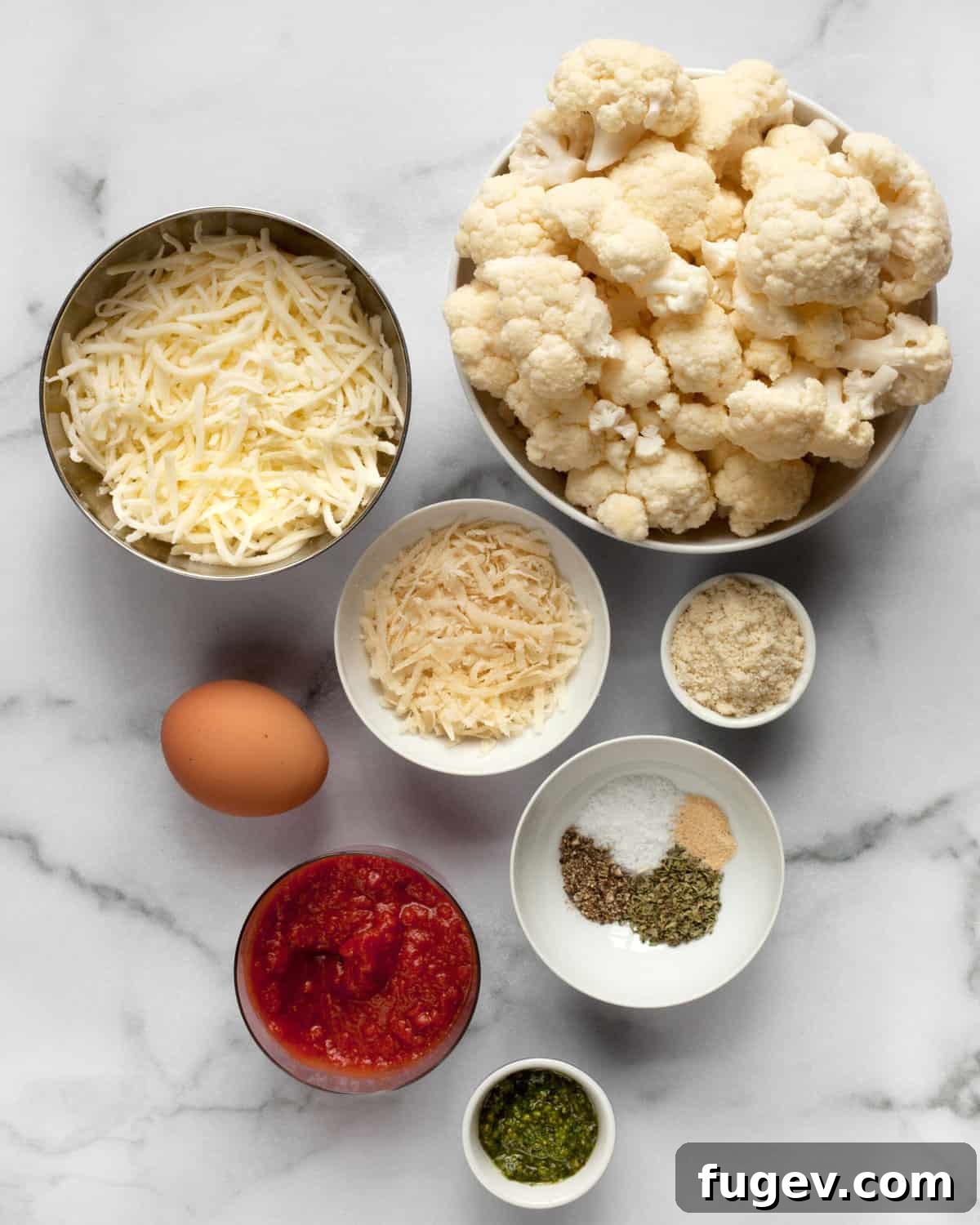 Power Cauliflower Crust 3 Various ingredients for cauliflower pizza, including fresh cauliflower florets, cheese, almond flour, an egg, pizza sauce, and herbs.