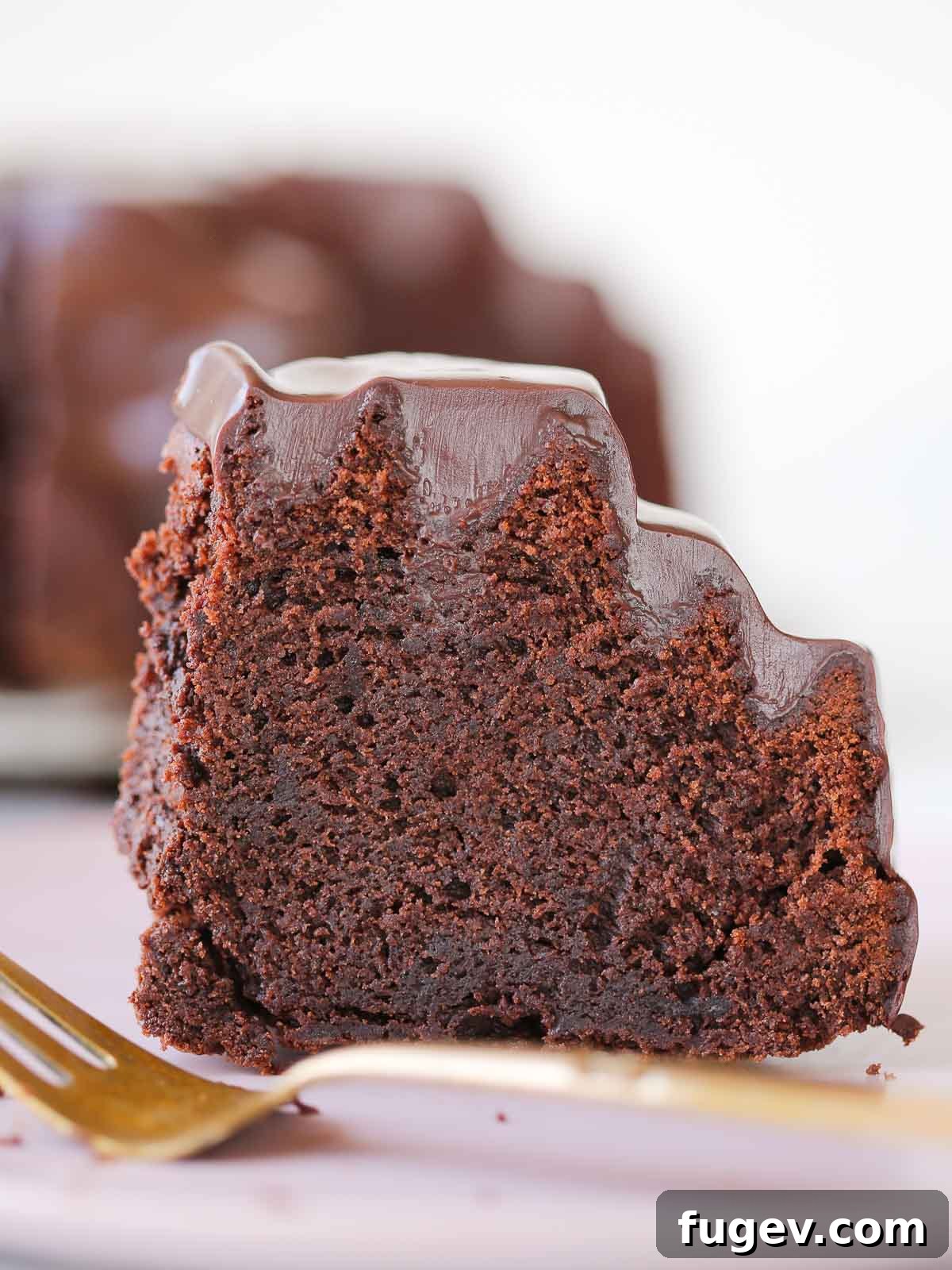 Decadent Chocolate Bundt 2 A perfectly sliced piece of moist chocolate bundt cake adorned with glistening chocolate ganache, presented on an elegant gold cake server, highlighting its rich texture and decadent appeal.