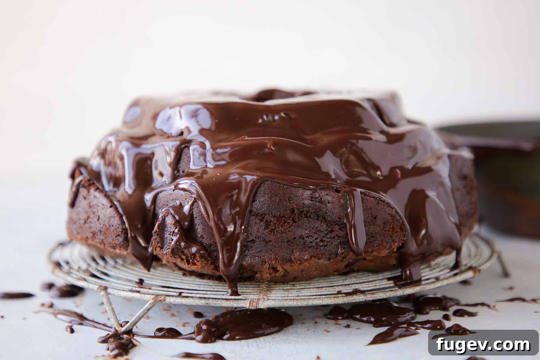 Decadent Chocolate Bundt 4 A rich chocolate bundt cake, still warm, with glistening chocolate ganache slowly dripping down its sides, resting on a vintage wire cooling rack.