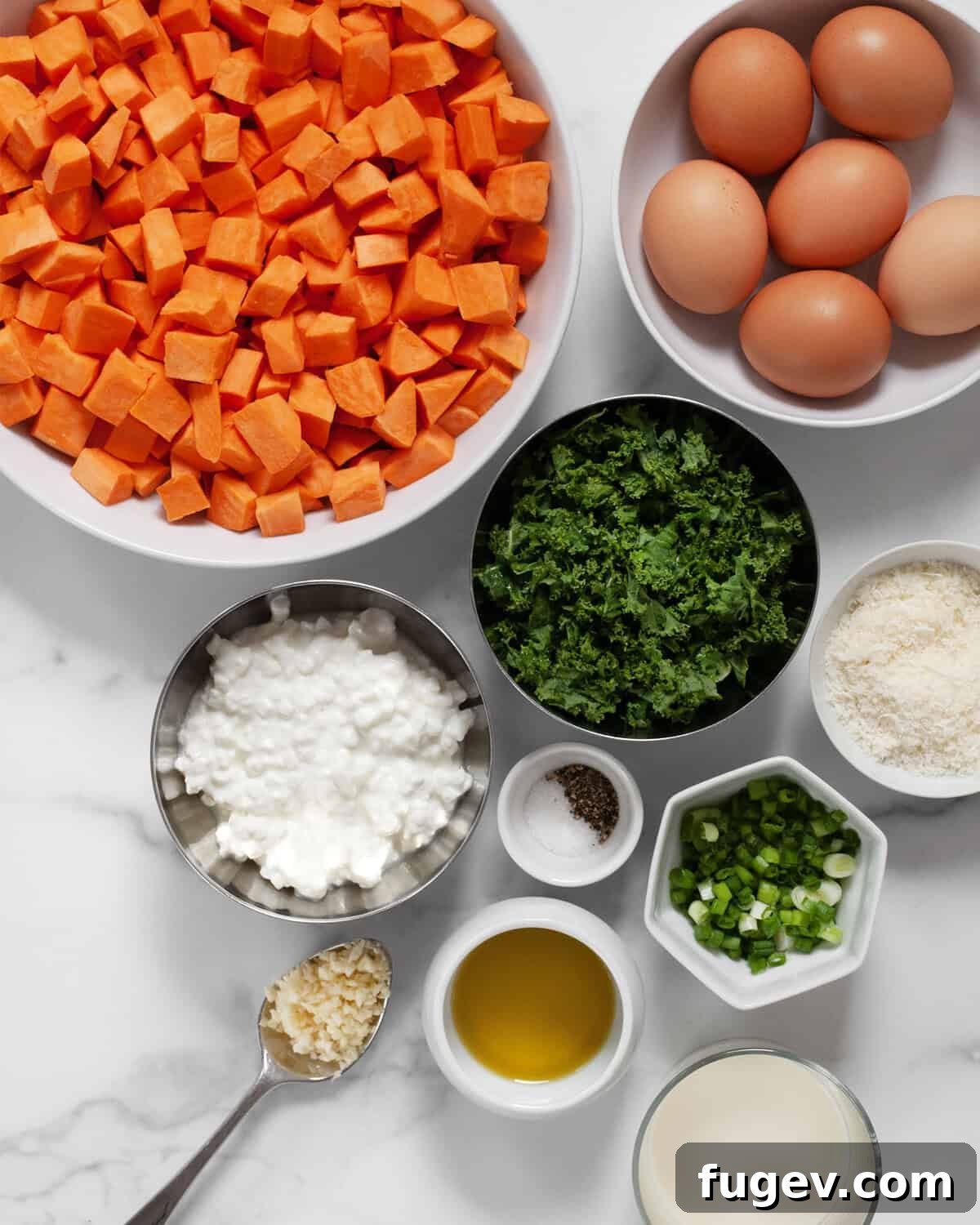 Arrangement of fresh ingredients including vibrant sweet potatoes, fresh kale, grated parmesan cheese, eggs, milk, creamy cottage cheese, olive oil, bright scallions, whole garlic cloves, and seasoning (salt and pepper).