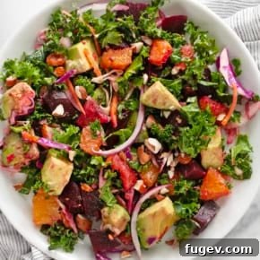 Colorful Roasted Beet and Orange salad with kale, avocado, red onion, and almonds, dressed in a zesty vinaigrette.