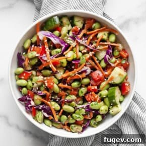 Fresh Edamame Salad with red cabbage, bell peppers, cucumbers, carrots, and edamame, tossed in a zesty tahini ginger dressing.