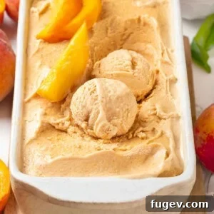 Scoops of fresh peach ice cream in a white loaf pan with slices of peaches.