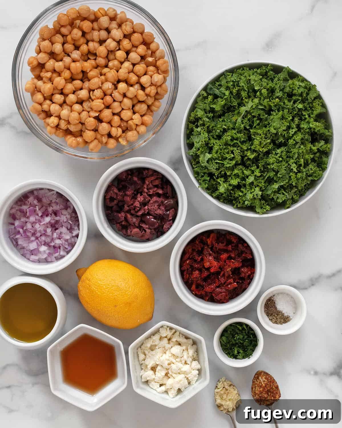 Green Goddess Chickpea & Kale Salad 3 A flat lay of fresh ingredients for kale chickpea salad including kale, chickpeas, red onions, sun-dried tomatoes, kalamata olives, parsley, lemon, feta, red wine vinegar, olive oil, mustard, garlic, salt, and pepper.