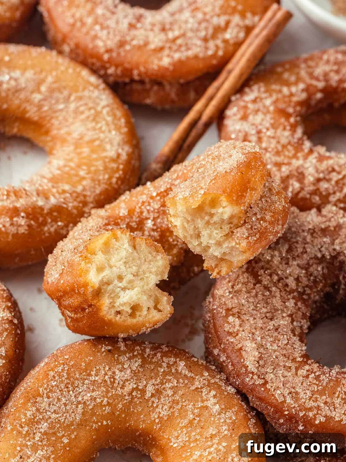 Harvest Apple Cider Donuts 2 A close-up of golden brown apple cider donuts stacked next to a cinnamon stick and a few star anise, emphasizing the cozy, autumnal flavor and inviting texture.