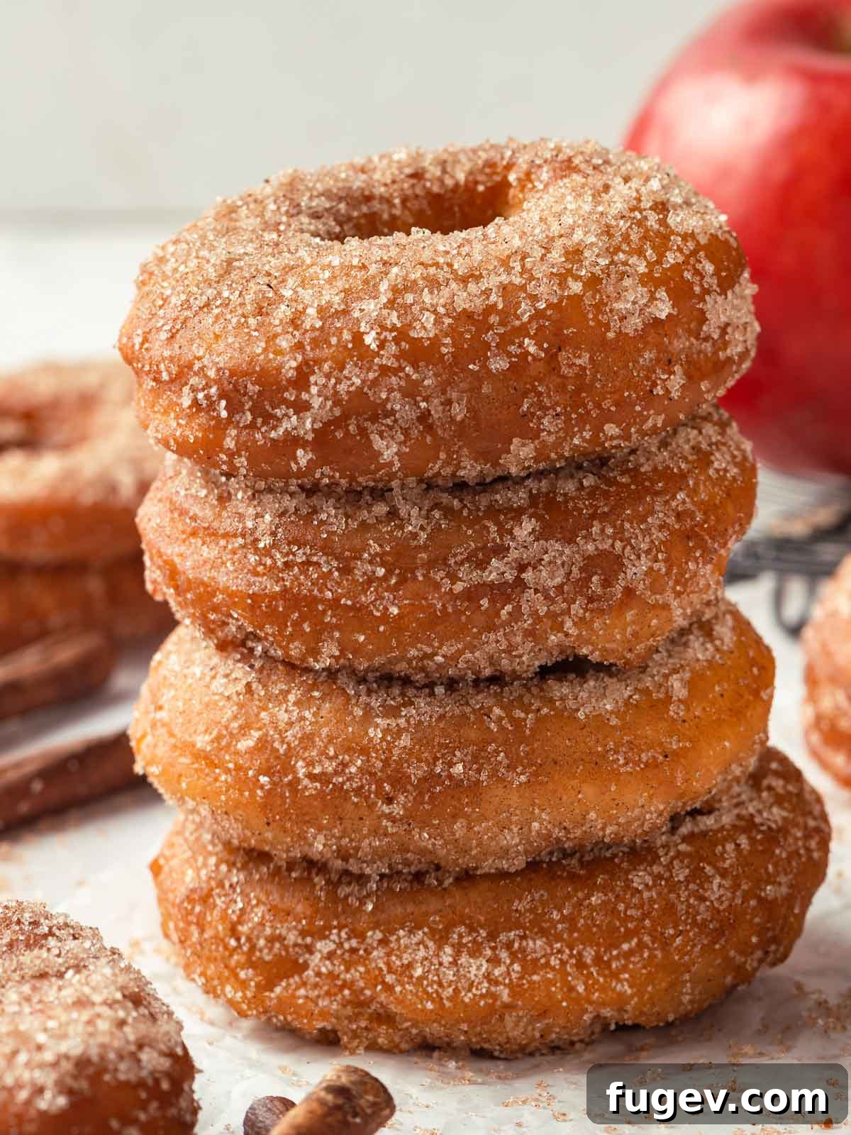 Harvest Apple Cider Donuts 3 Four golden-brown apple cider donuts stacked on a rustic wooden surface, showcasing their fluffy, sugary appearance and perfect shape.
