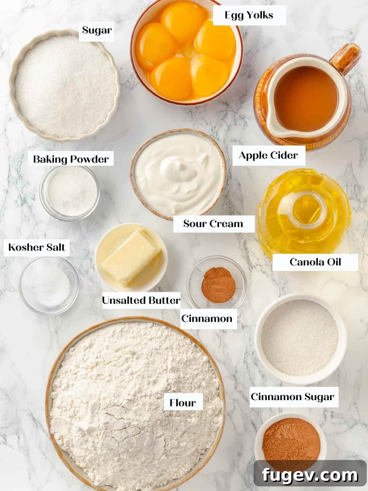Harvest Apple Cider Donuts 4 Ingredients for apple cider donuts carefully laid out on a clean white marble countertop, featuring flour, sugar, butter, eggs, apple cider, and spices.