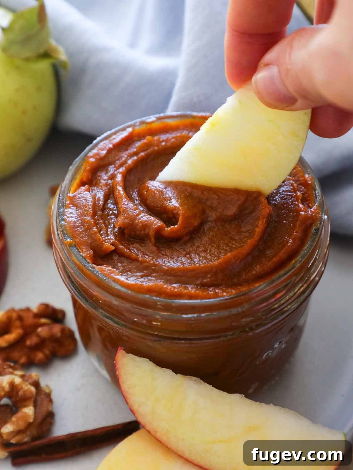Cozy Spiced Pumpkin Butter 2 A hand scooping thick, spiced pumpkin butter from a glass jar, with a fresh apple slice ready for dipping.