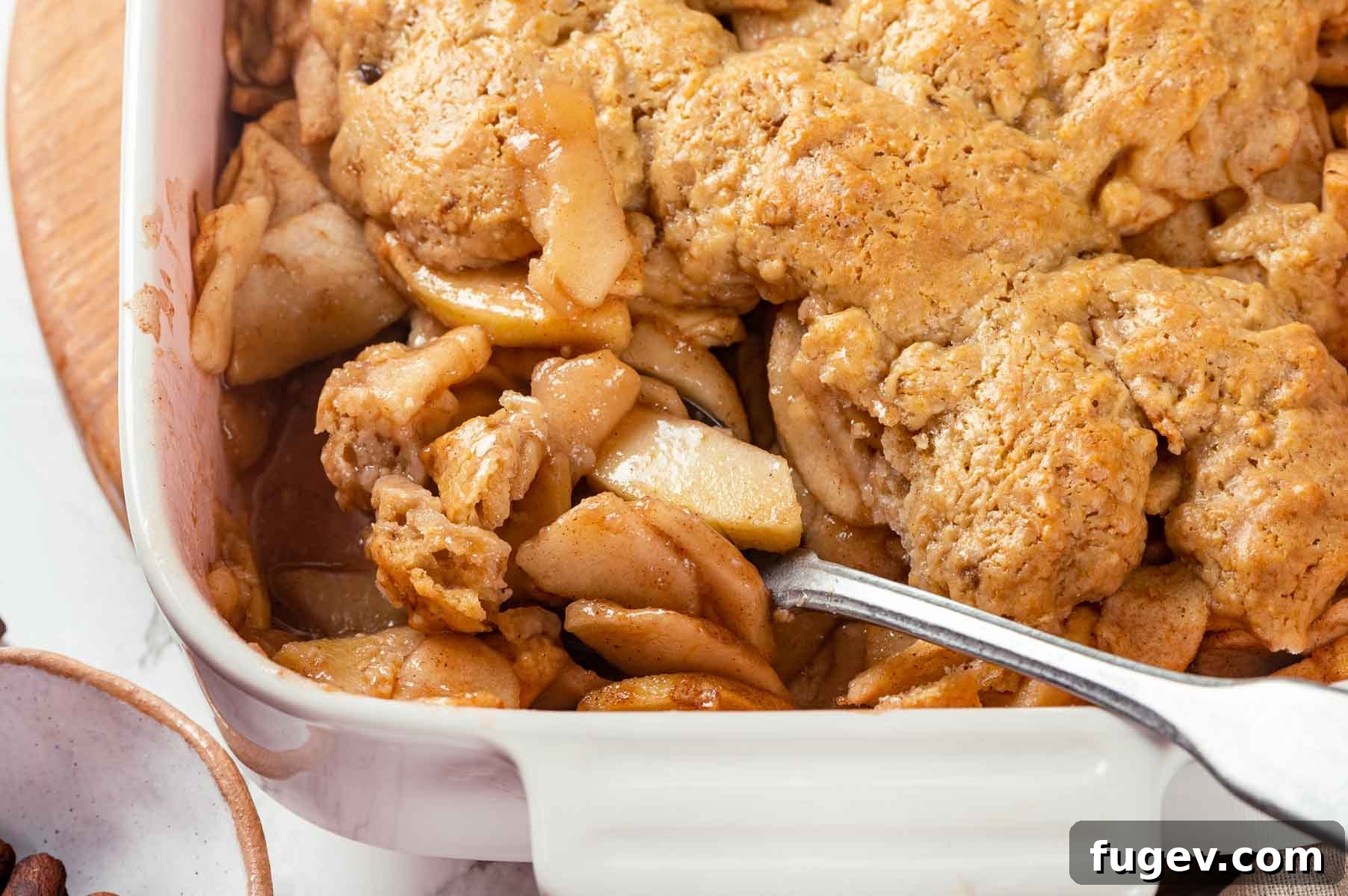 Cozy Apple Cobbler Magic 3 A close-up view of a baked apple cobbler, showing the soft, spiced apple filling bubbling beneath a golden-brown biscuit topping, revealing its delicious interior.