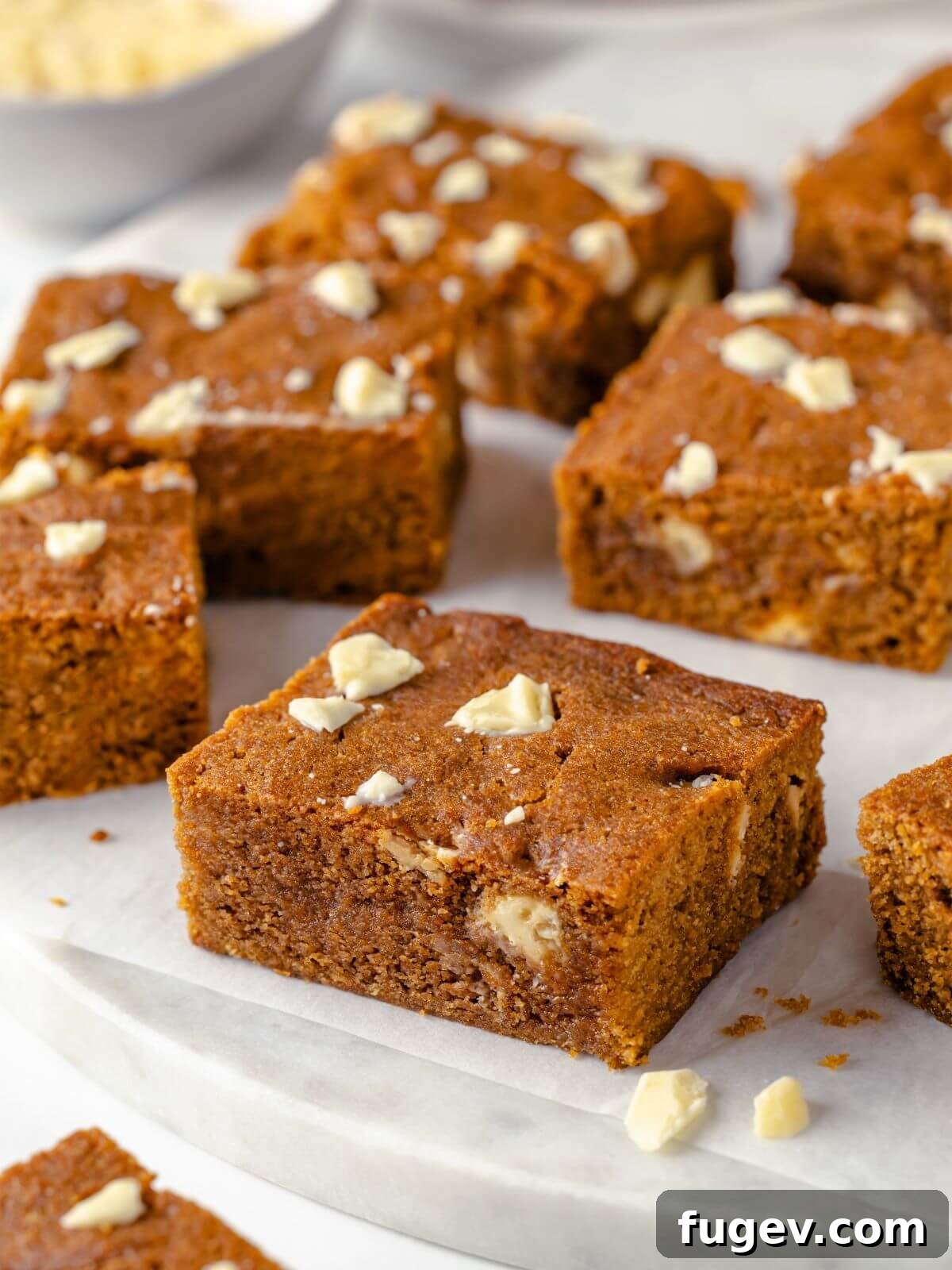 Chewy Gingerbread Blondies 2 Soft, chewy gingerbread blondies topped with white chocolate chunks, artfully arranged on a white marble surface, highlighting their rustic charm and delectable texture.