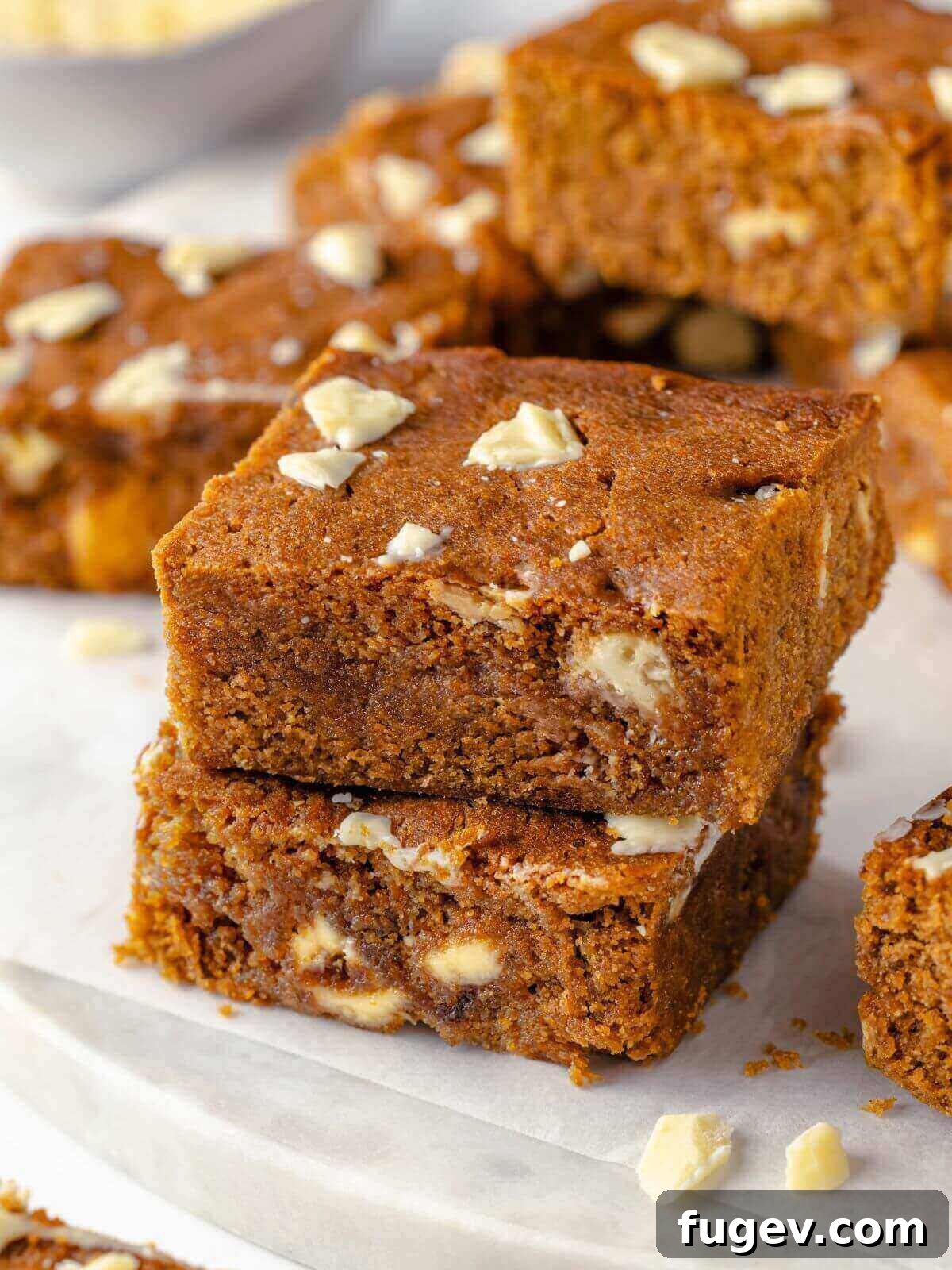 Chewy Gingerbread Blondies 13 A captivating close-up of a gingerbread blondie, showcasing its soft, moist interior and generous distribution of melted white chocolate chunks, inviting a delicious bite.