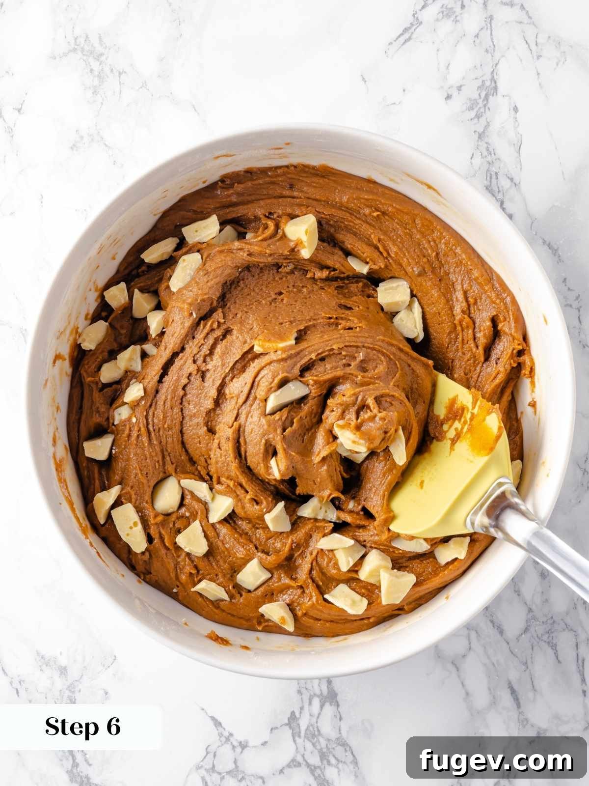 Chewy Gingerbread Blondies 10 A mixing spatula gently folding generous white chocolate chips into the thick, spiced gingerbread blondie batter in a clear glass bowl.