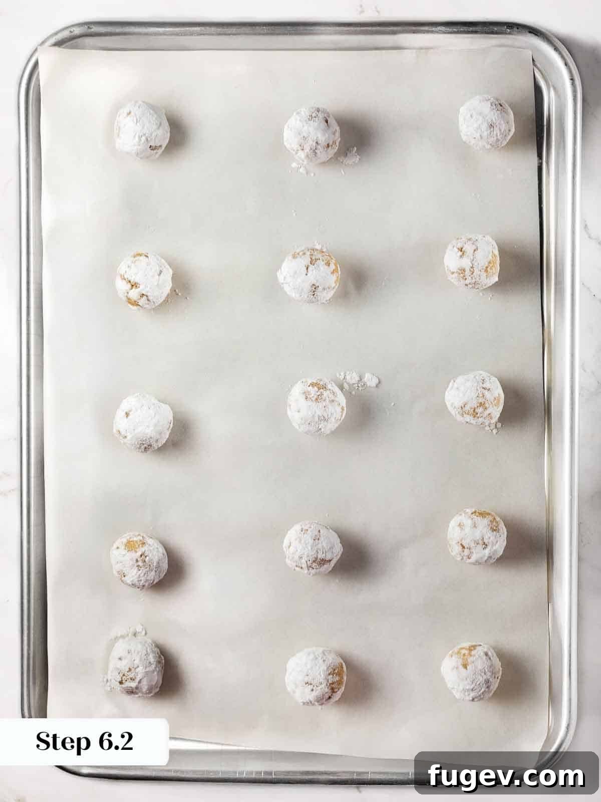 Italian Almond Amaretti 10 Powdered sugar-coated amaretti cookie dough balls arranged on a parchment-lined baking sheet, ready for the oven.