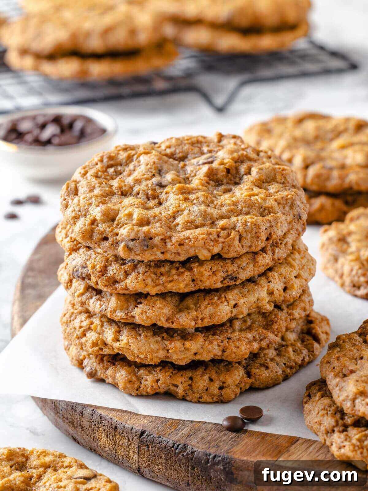 Hearty Cowboy Cookies 2 A stack of golden-brown cowboy cookies on a rustic wooden board, surrounded by loose chocolate chips and oats, highlighting their rich texture and abundant mix-ins.