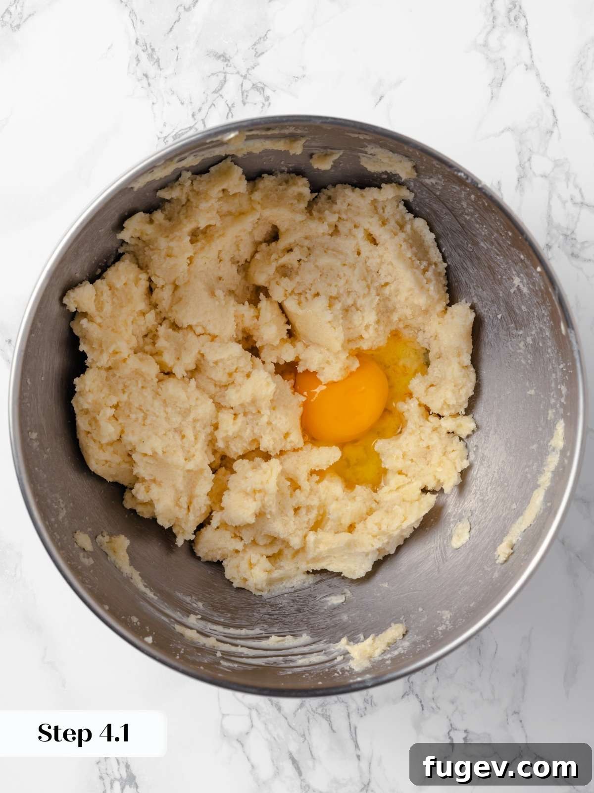 Hearty Cowboy Cookies 9 Two large eggs being cracked and added one by one into the creamed butter and sugar mixture in a mixing bowl for cowboy cookie dough.