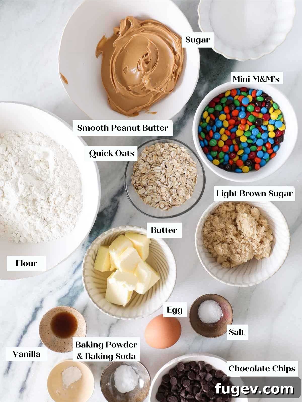 Ultimate Monster Cookies 4 A flat lay of monster cookie ingredients on a white marble counter, including oats, peanut butter, and M&Ms.