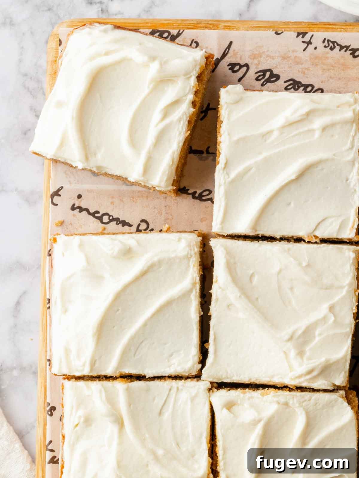Luscious Banana Cake with Tangy Cream Cheese Frosting 11 Freshly baked banana cake with cream cheese frosting, neatly cut into squares and displayed on parchment paper.