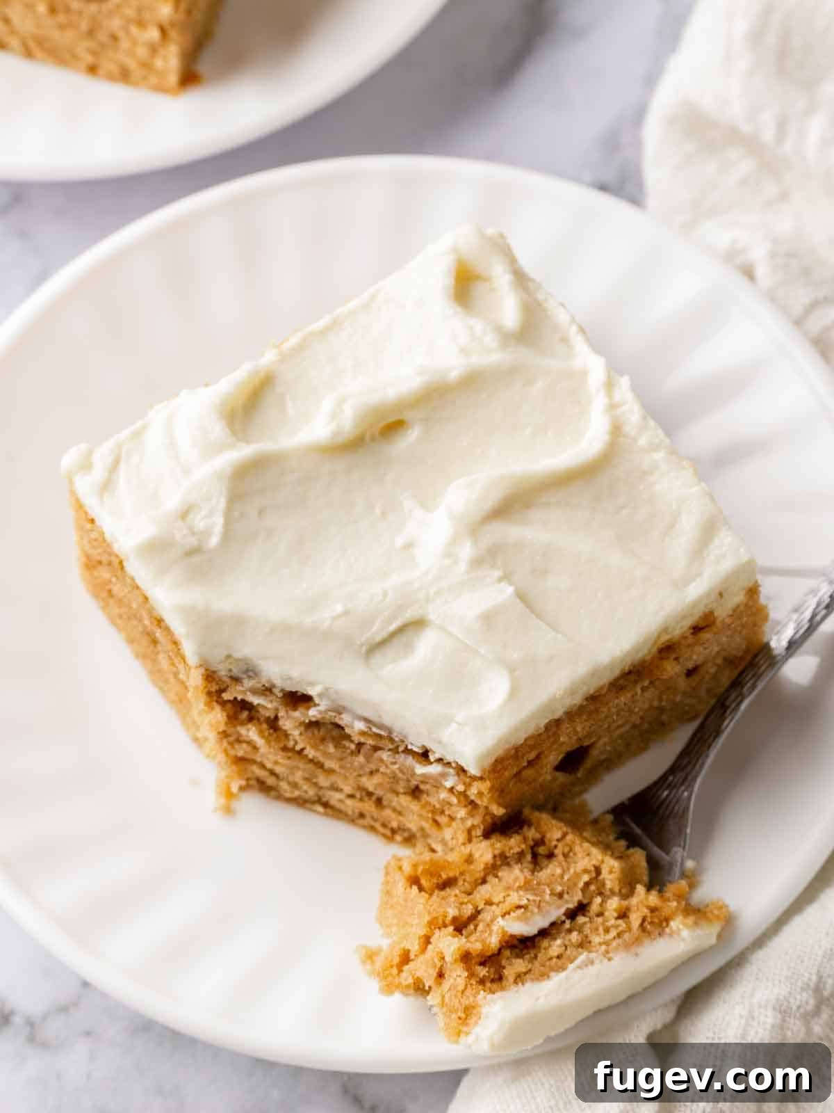 Luscious Banana Cake with Tangy Cream Cheese Frosting 12 A tantalizing slice of banana cake with fluffy cream cheese frosting, served on a plate with a fork, ready to be enjoyed.