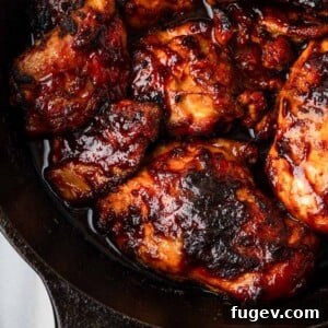 Baked BBQ chicken glistening with sauce in a black cast iron skillet.