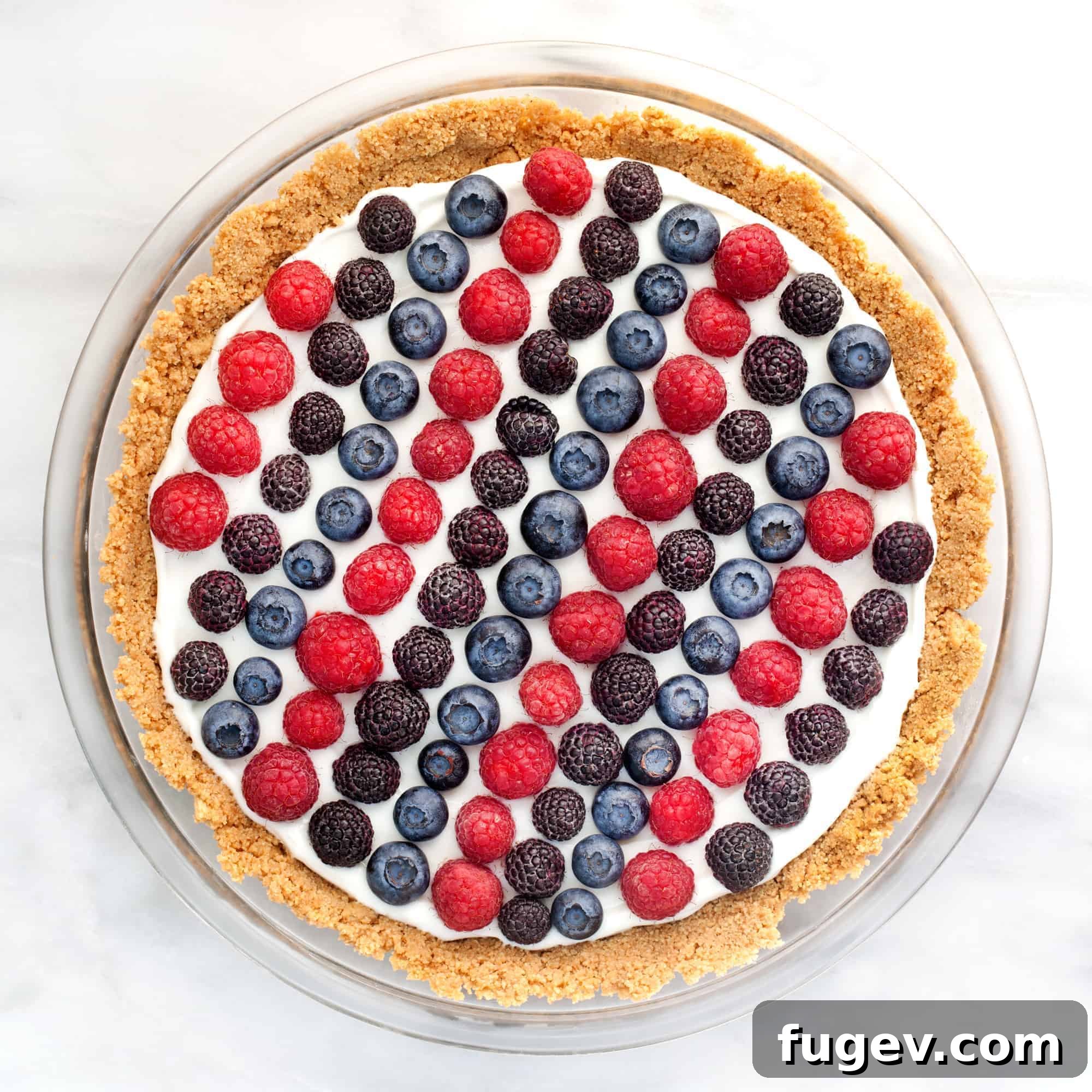 No-Bake Berry Yogurt Bliss 2 Vibrant No-Bake Berry Yogurt Pie garnished with fresh red raspberries, plump blueberries, and sliced strawberries, set on a rustic wooden surface.