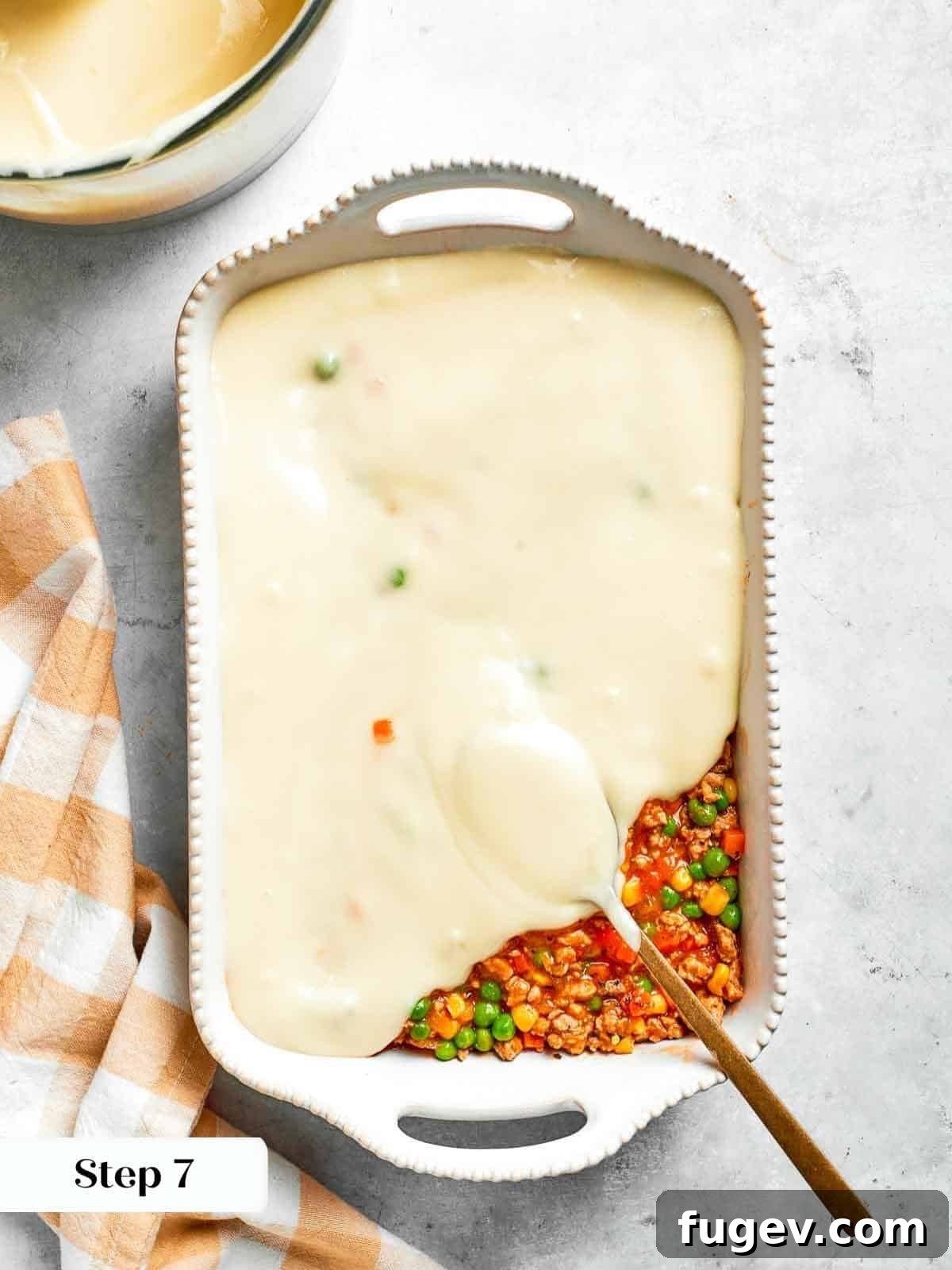 Golden Chicken Potato Bake 18 A spoon evenly layering mashed potatoes over the shepherd’s pie filling before baking.