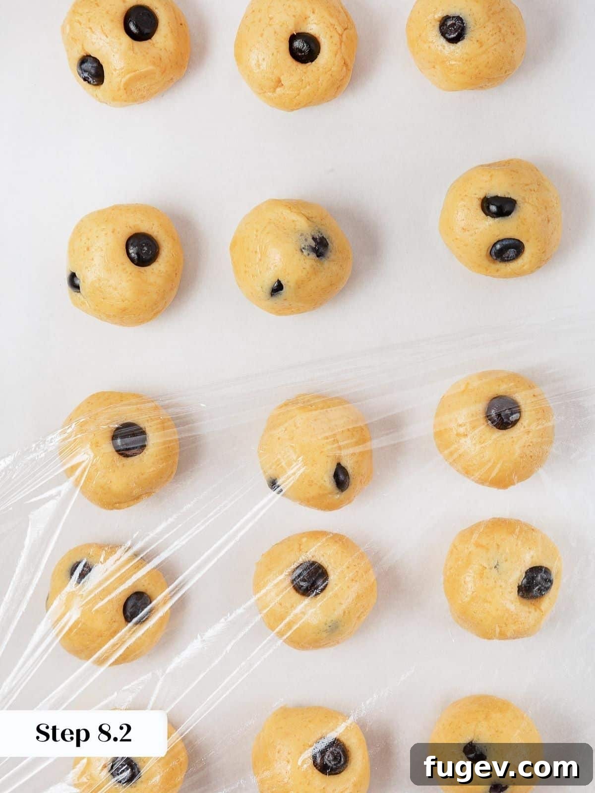 Bright Lemon Blueberry Delights 16 Portioned cookie dough on a baking sheet, meticulously wrapped in plastic wrap to chill before baking.