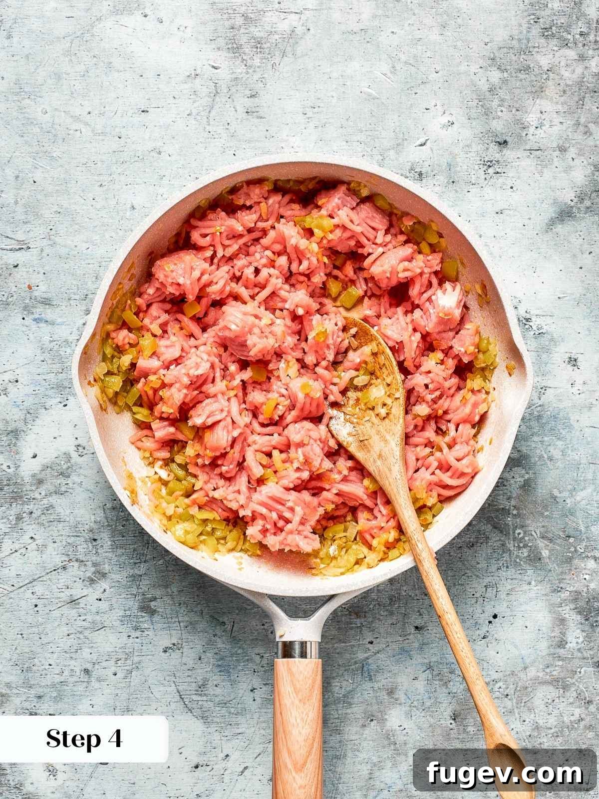 Homestyle Turkey Sloppy Joes 7 A wooden spoon breaking up the browned ground turkey meat as it cooks in the skillet.