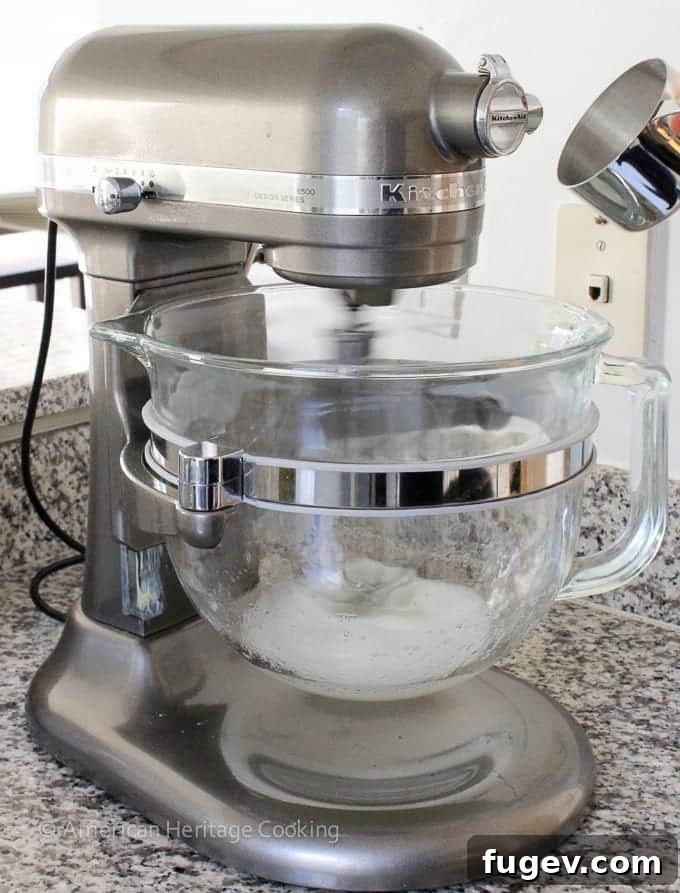 A silver stand mixer with a clear bowl and egg whites in the bottom, ready to be whipped into meringue.