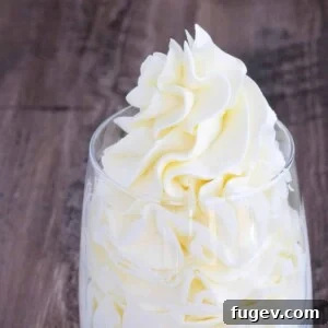 Cleanly piped Italian meringue buttercream in a clear glass, with a dollop on top, ready for serving.